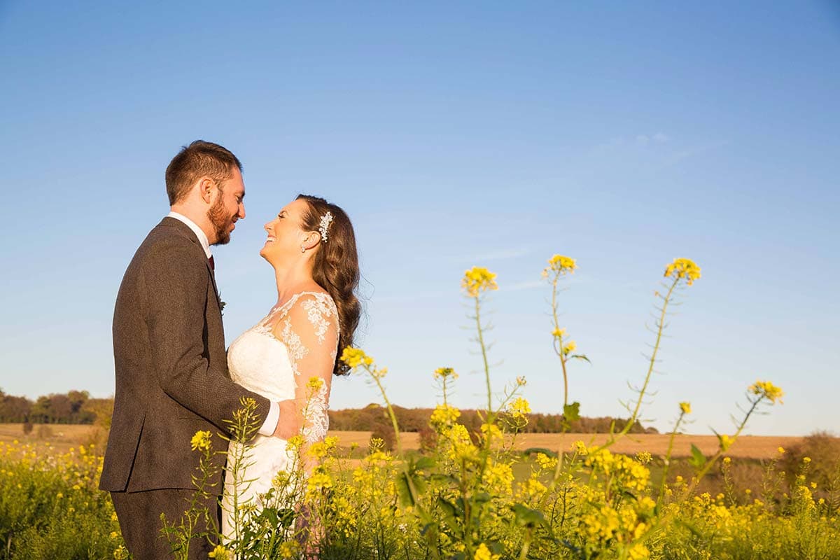 Bride and Groom stood in a reap seed field looking at each other