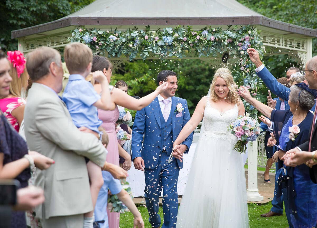 bride and groom walking through confetti for their outdoor wedding ceremony at Lainston House in Winchester, Hampshire