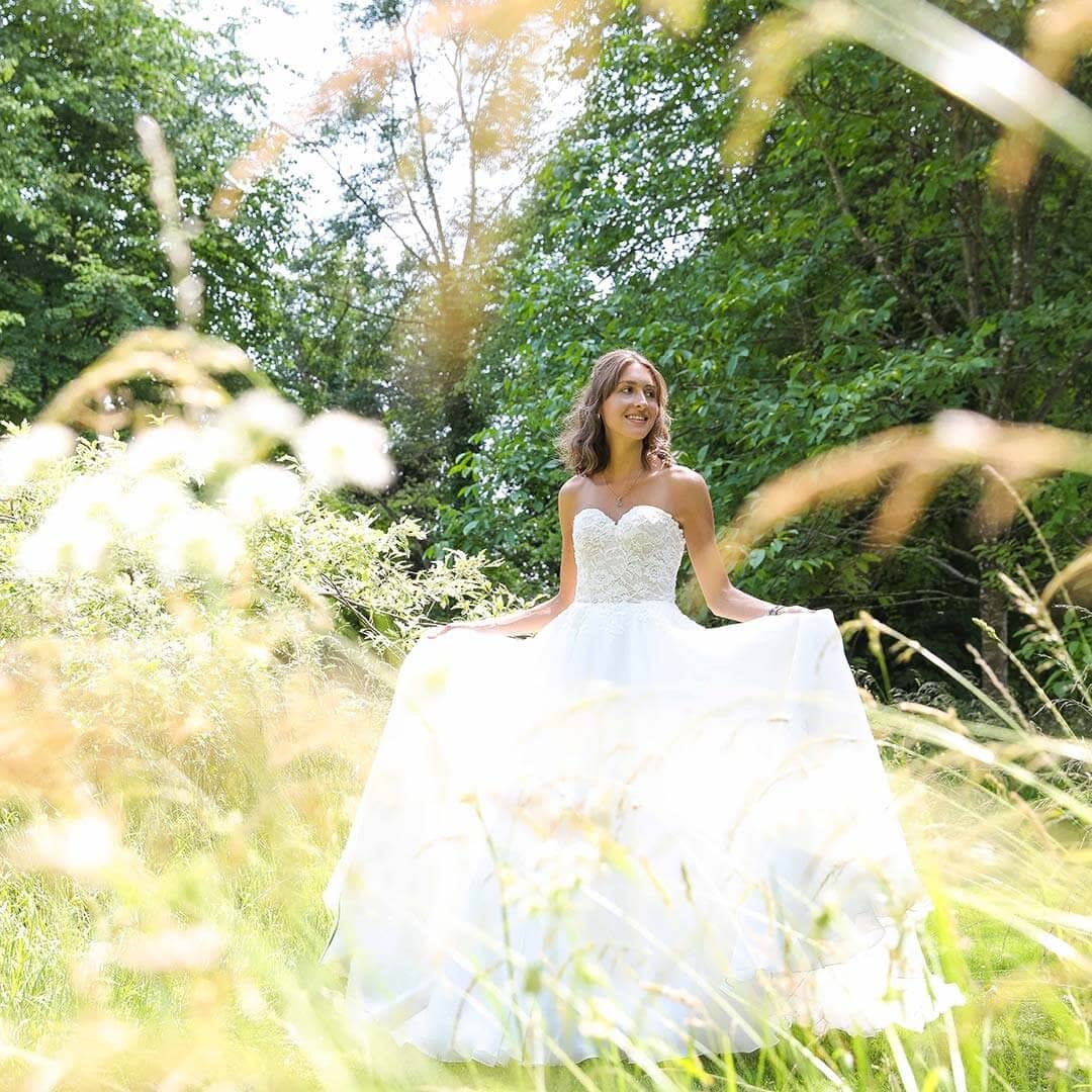 A bride in a field of long grass holding out her wedding dress